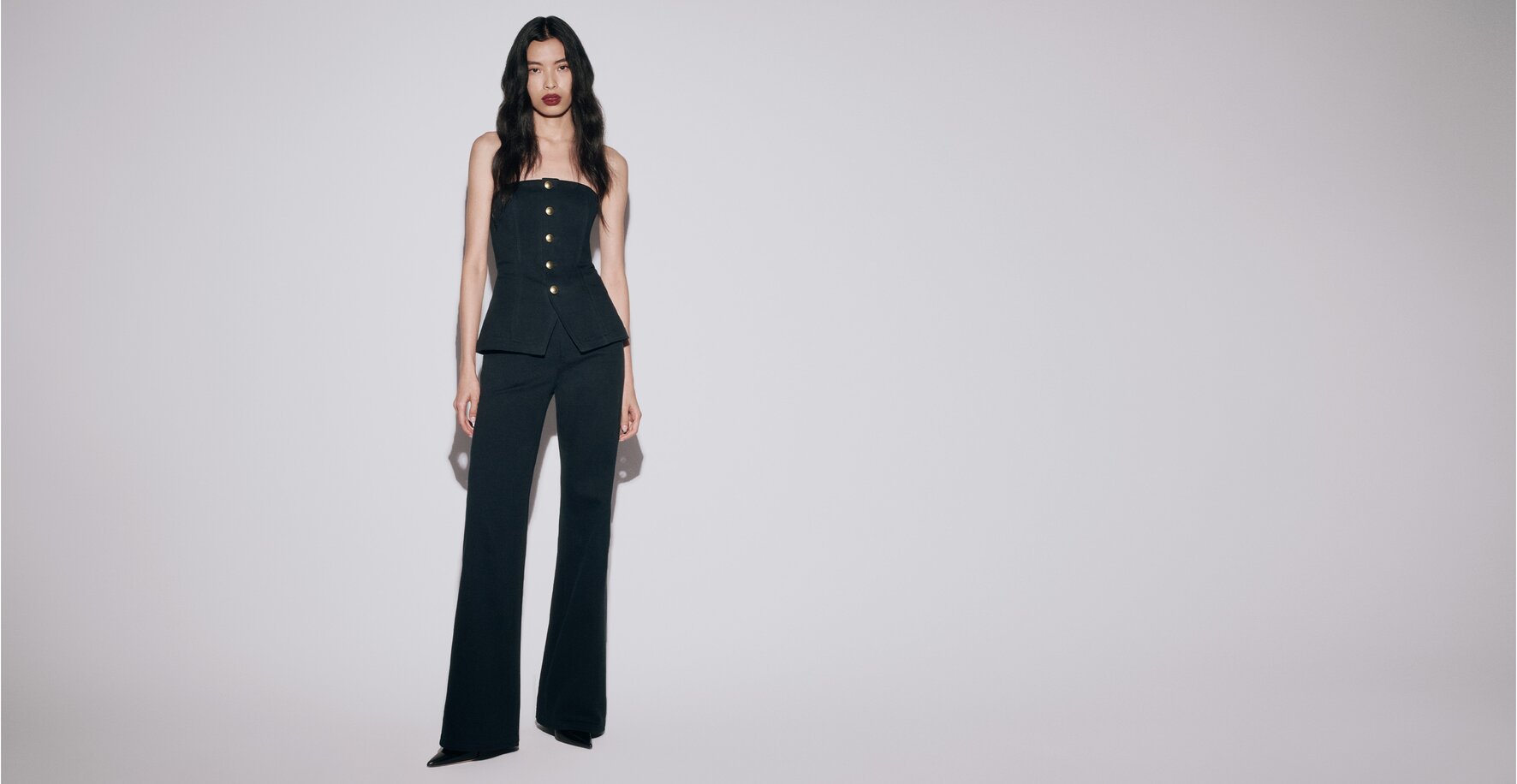 Woman wearing a dark wash denim strapless top with gold buttons, matching dark wash jeans, and black pumps