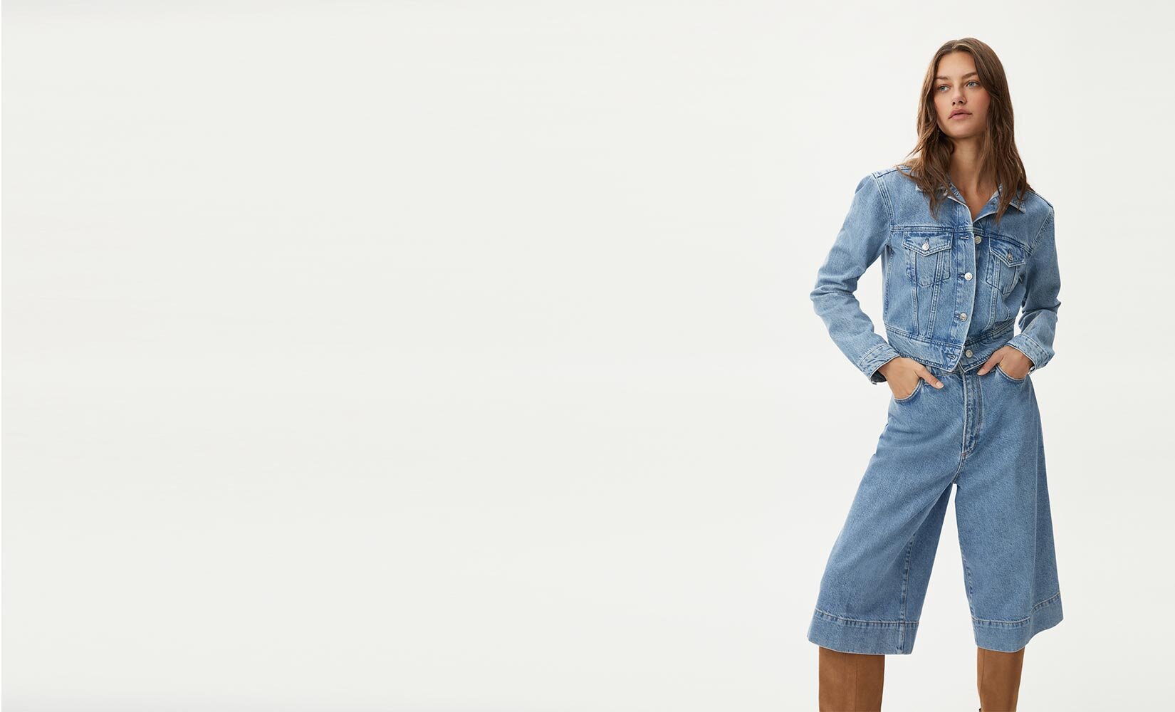 Woman wearing a light wash denim on denim jacket & gaucho set with tall brown suede boots