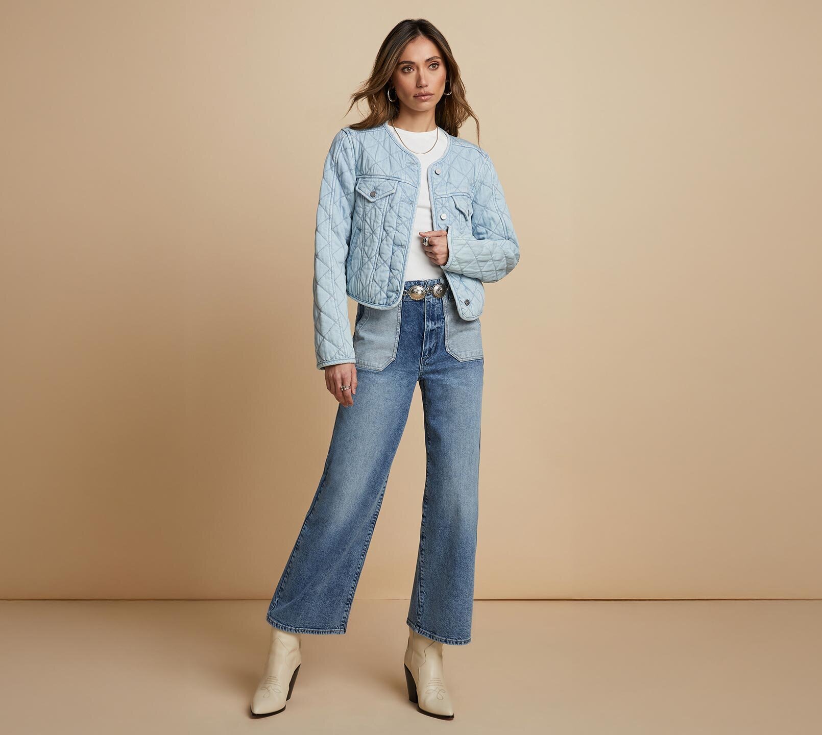 Woman standing a light blue quilted jacket, white tee, medium wash jeans and bone ankle boots