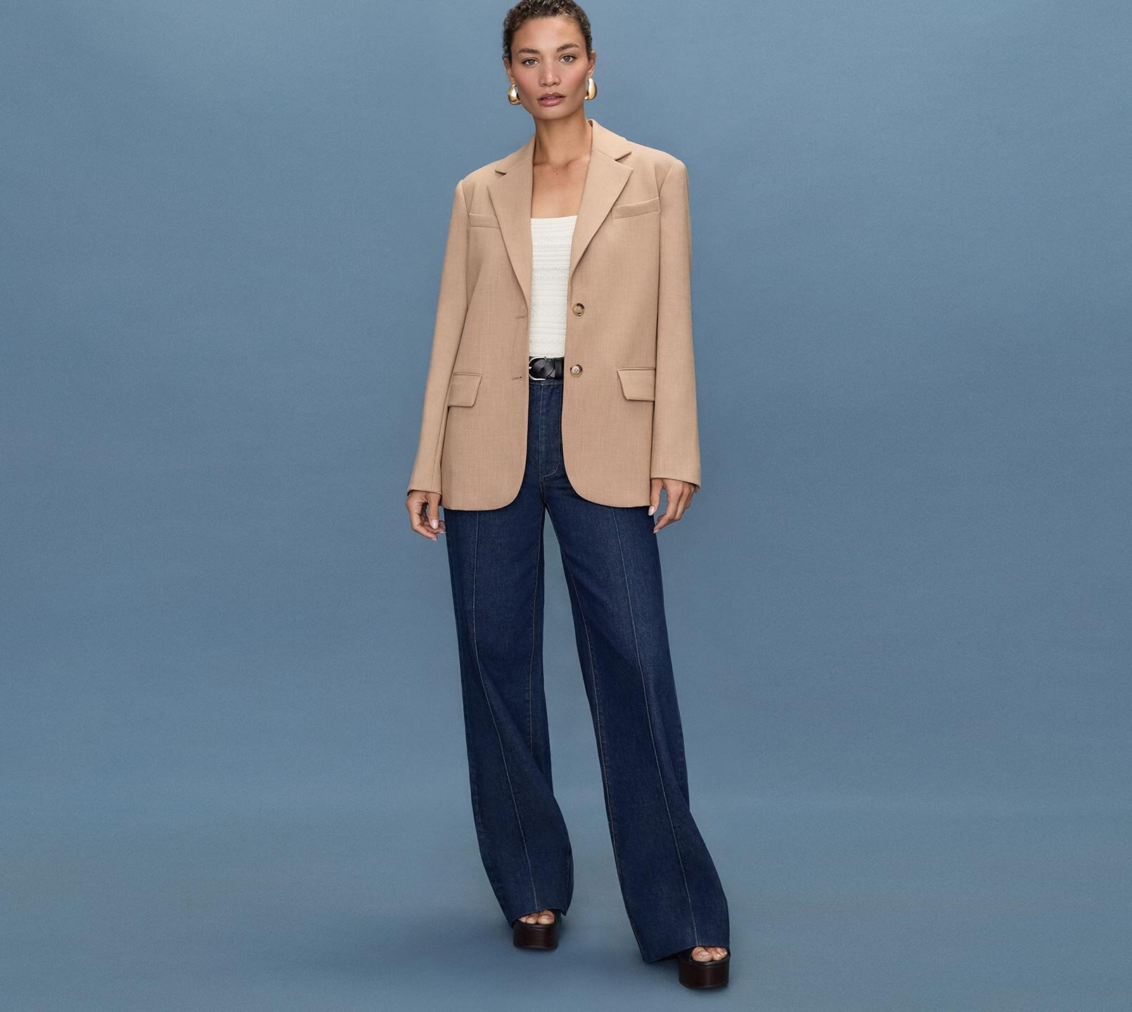 Woman standing a light blue quilted jacket, white tee, medium wash jeans and bone ankle boots