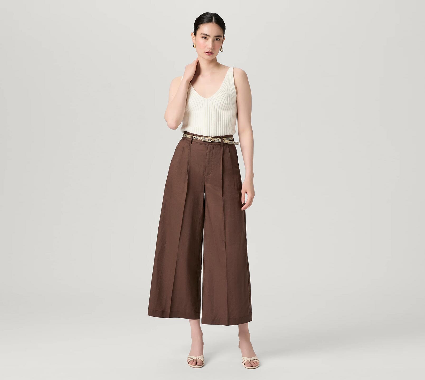 Woman wearing an ivory sweater tank, brown wide leg pants, snake-printed belt and bone sandals