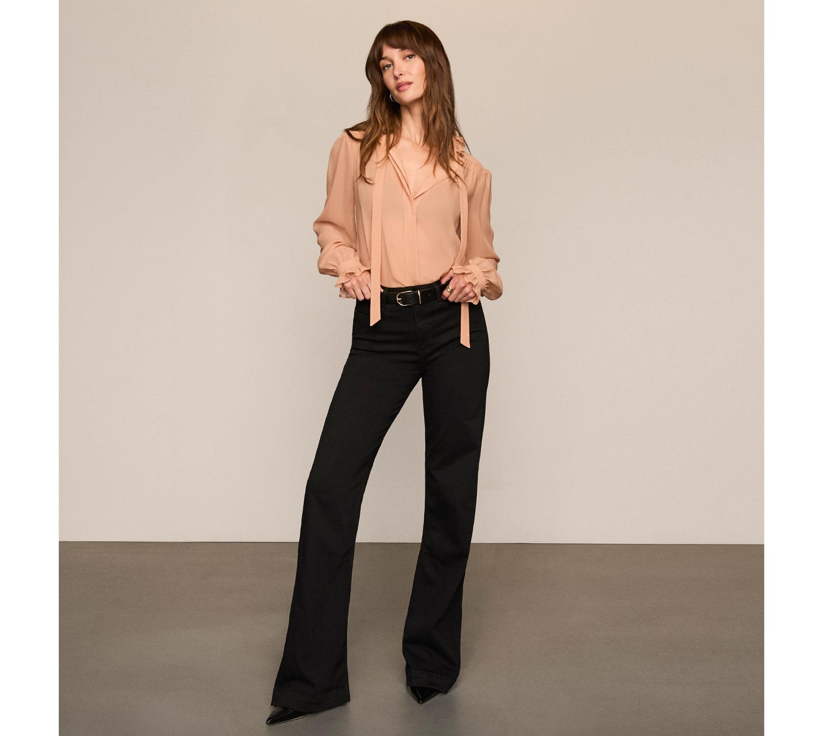Woman wearing a ballet pink long sleeve blouse with black jeans, a black belt, and black pumps