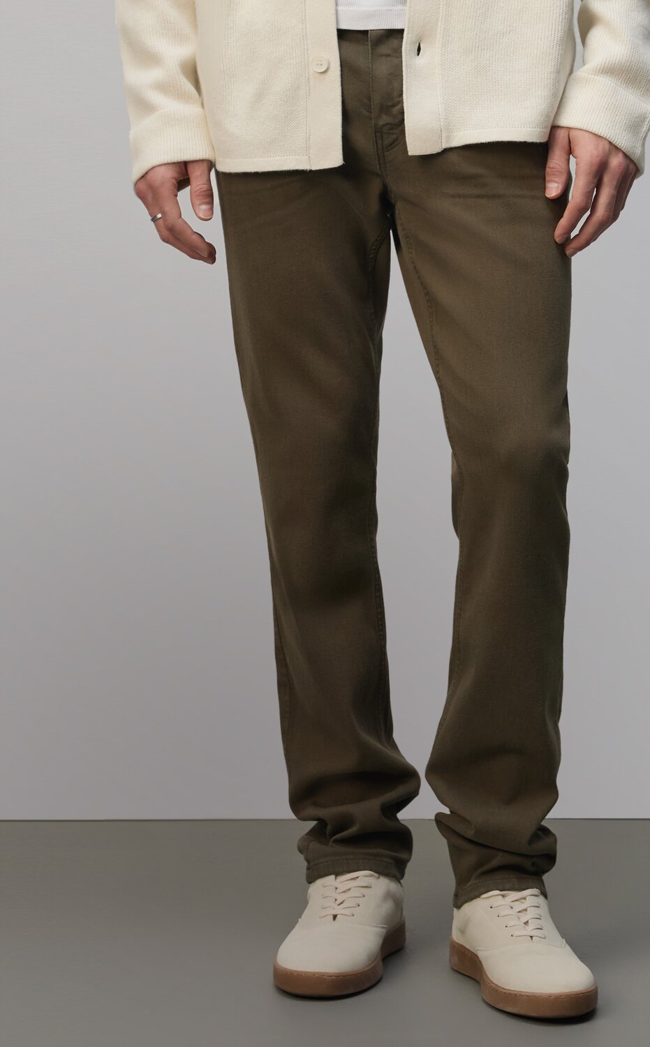 Man wearing a cream cardigan over a white tee, dark olive green jeans, and cream sneakers