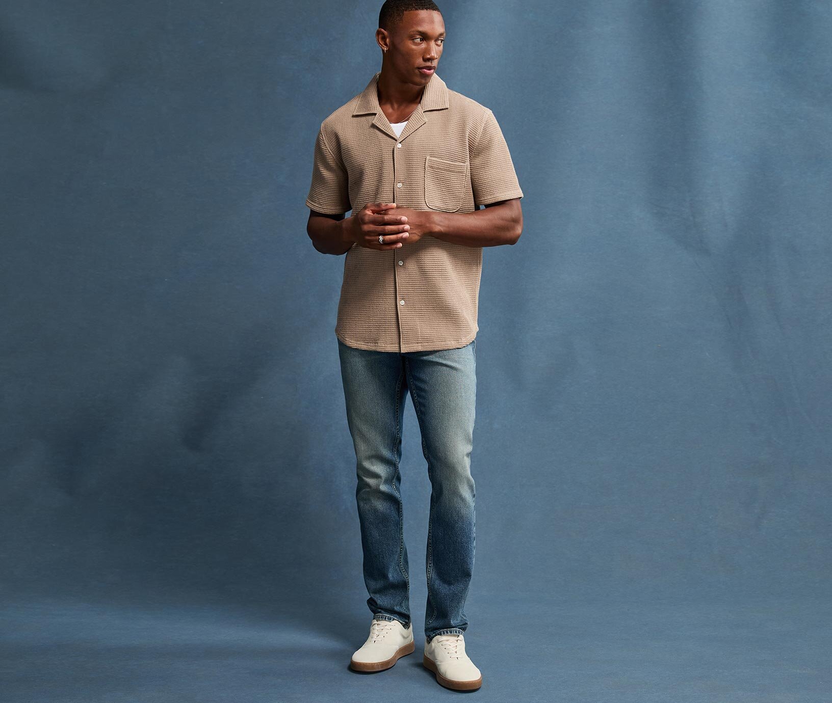 Man wearing an ivory short sleeve button down sweater shirt, light wash relaxed jeans & taupe suede loafers