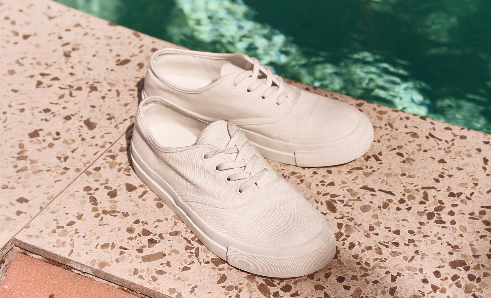 A pair of white canvas sneakers by the pool