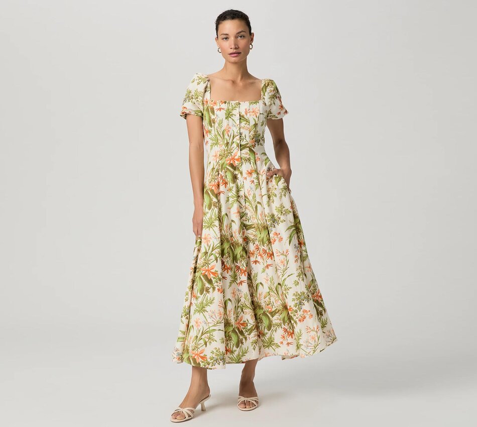 Woman wearing an ivory, orange, and green tropical floral printed midi dress and bone sandals