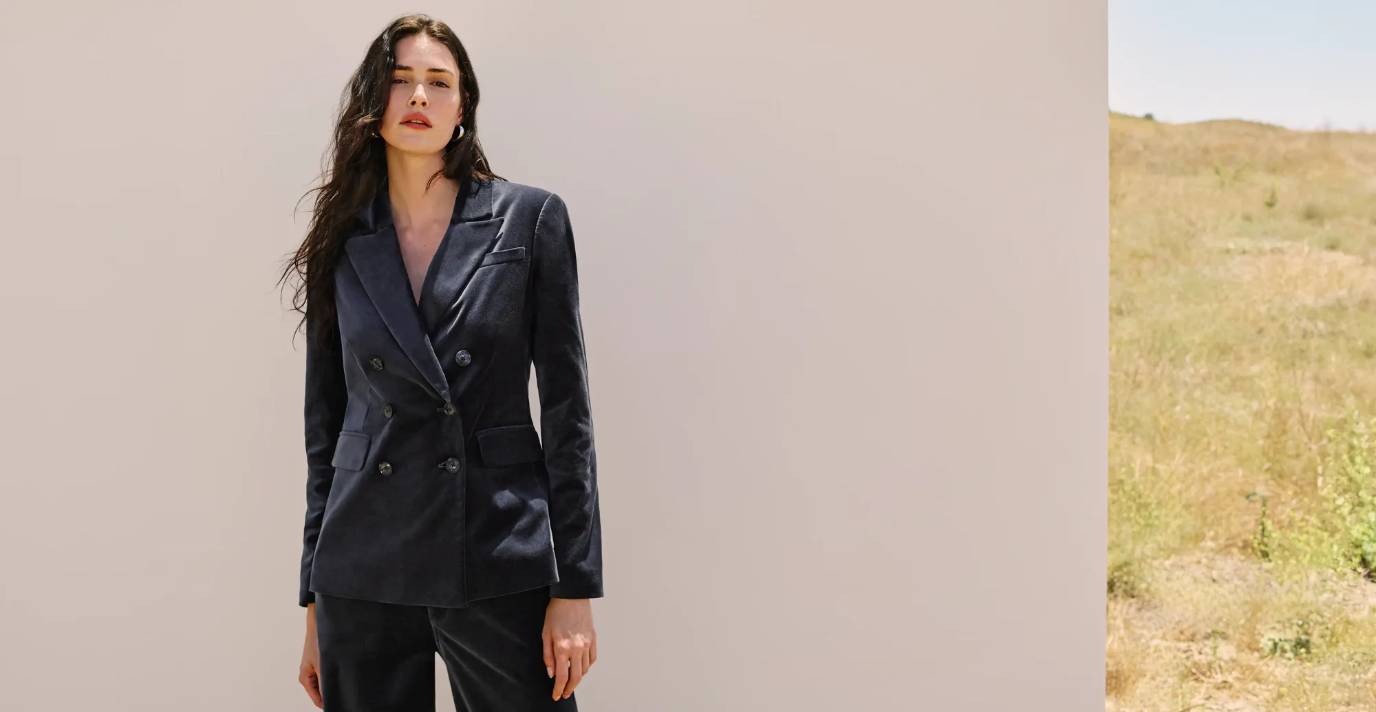 Woman standing outside in front of a white backdrop wearing a navy blue velvet suiting set