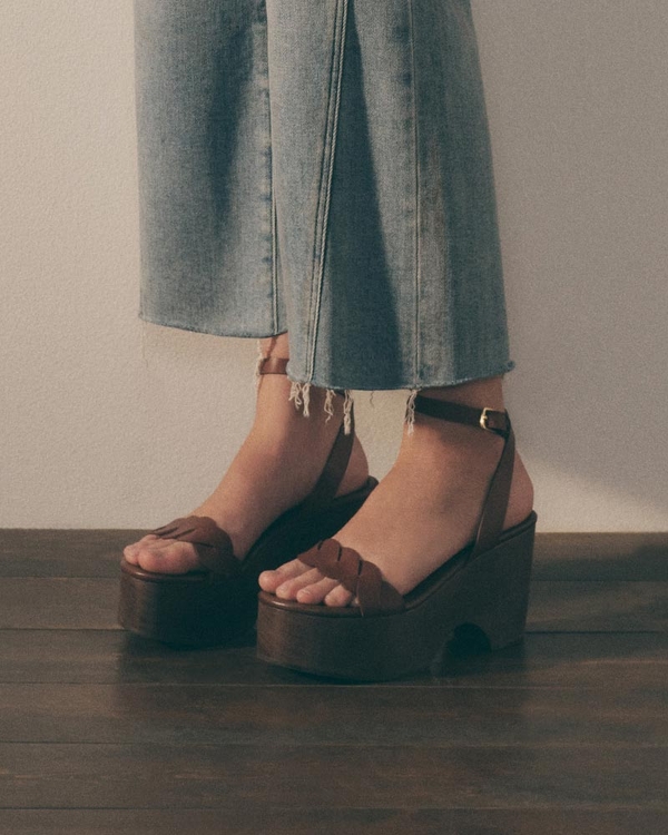 Flat lay of white lattice leather Mary Jane flats with a buckle strap on a neutral background.