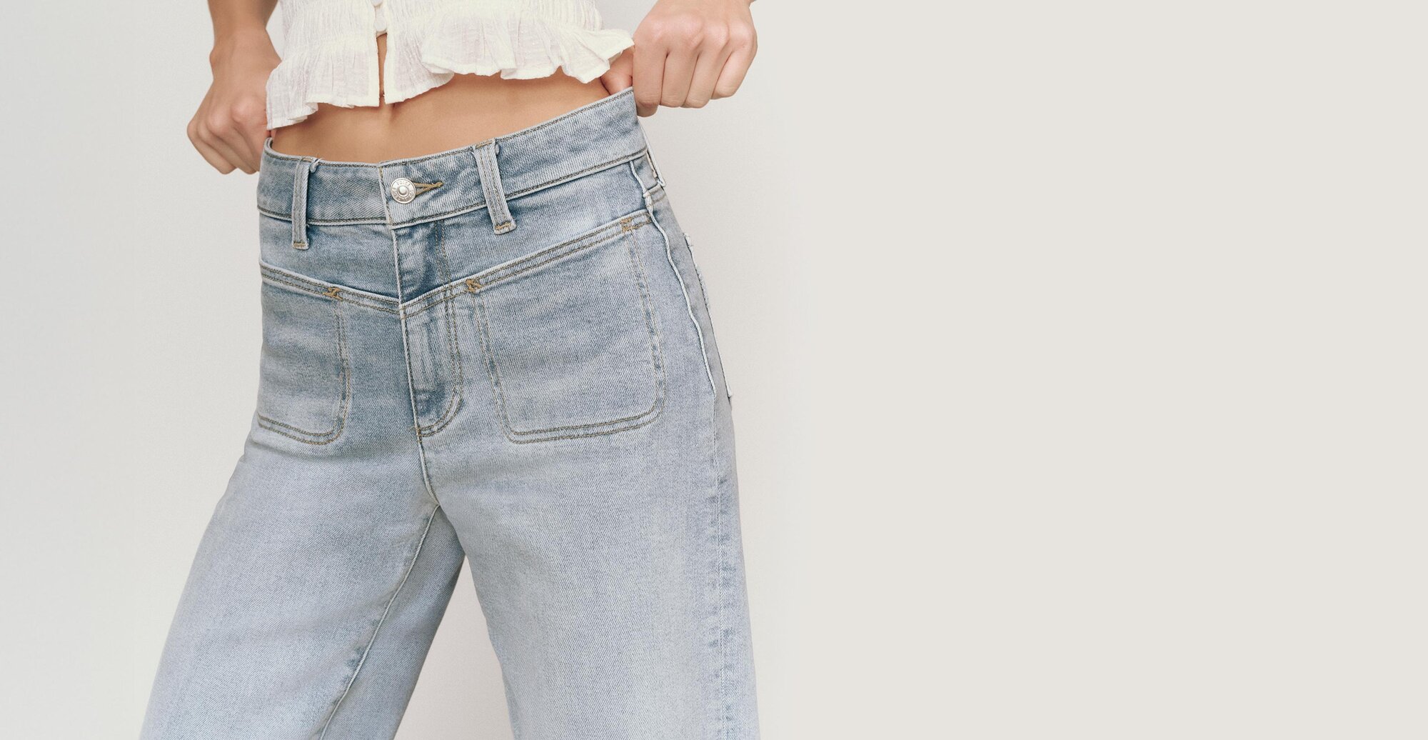 Woman wearing light wash high rise jeans in front of a grey backdrop.