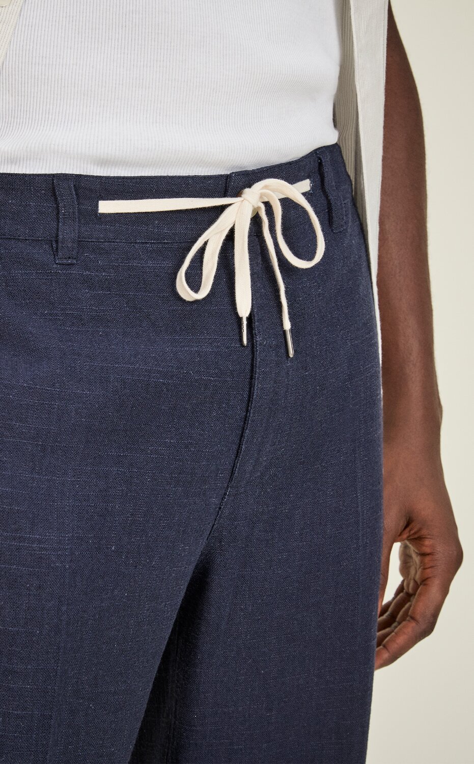 Close-up of navy drawstring pants with a white tie waist, styled with a white shirt.