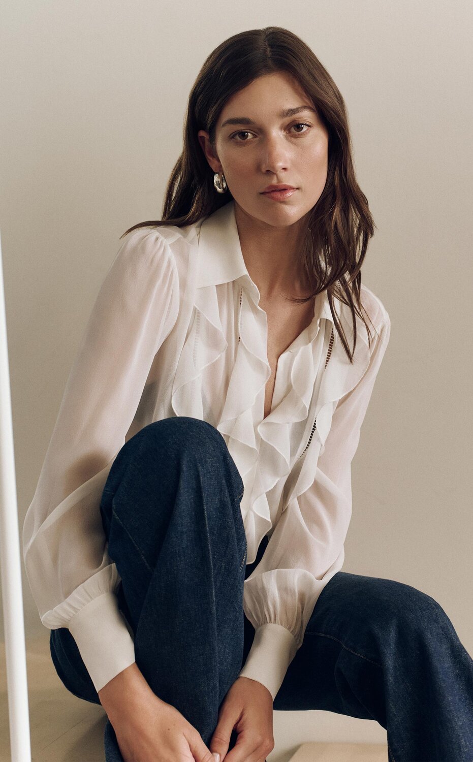 Woman wearing a white ruffle blouse and dark wash jeans