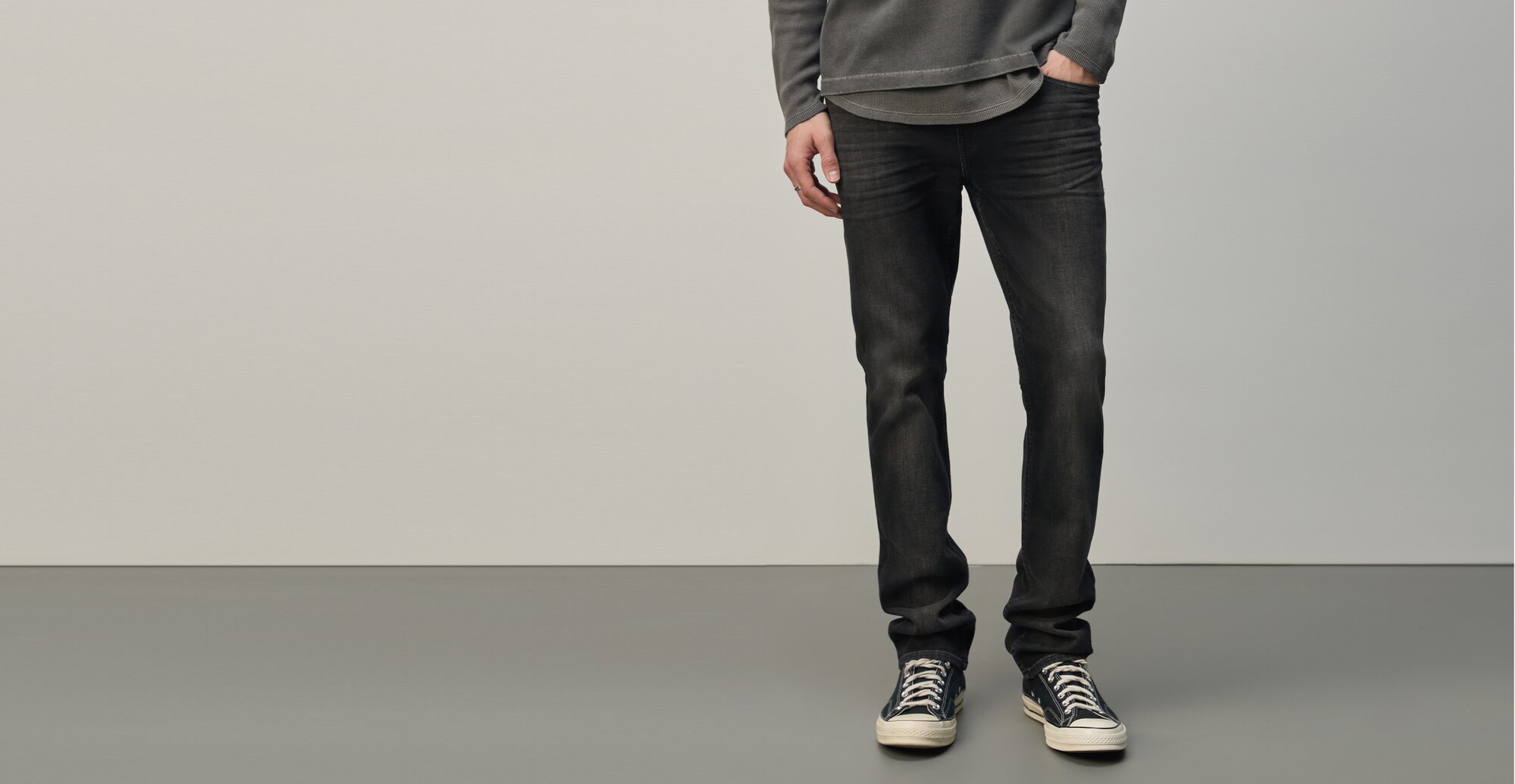 Man wearing a grey henley layered over a grey shirt, washed black jeans, and black sneakers