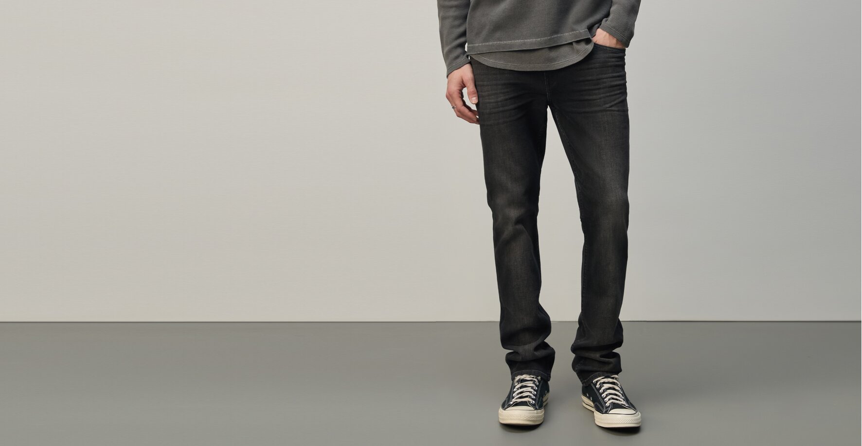 Man wearing a grey henley layered over a grey shirt, washed black jeans, and black sneakers