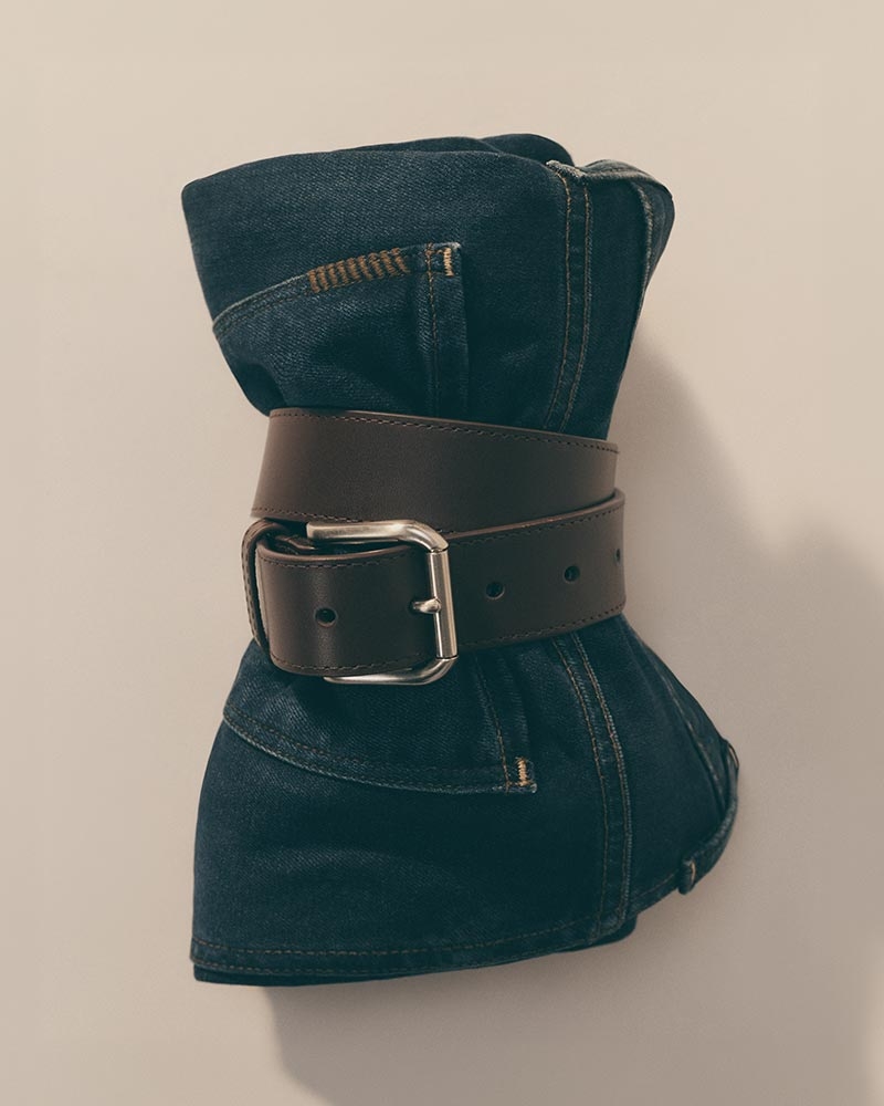 A pair of dark denim jeans rolled and held closed by a brown leather belt with silver buckle