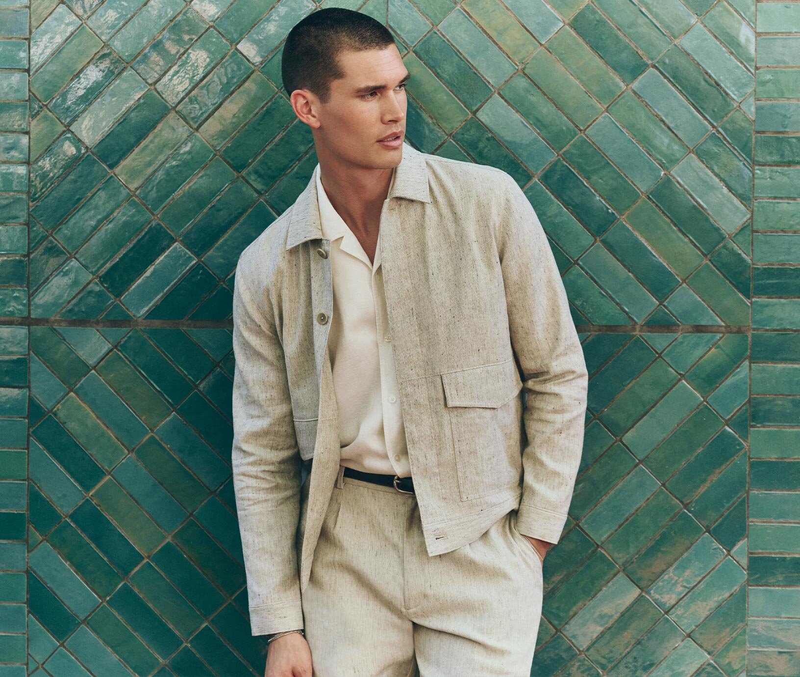 Man wearing an ivory short sleeve button down sweater shirt, light wash relaxed jeans & taupe suede loafers