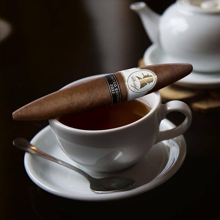 A premium cigar rests on the rim of a teacup filled with tea, showcasing an elegant contrast of flavors and indulgence.