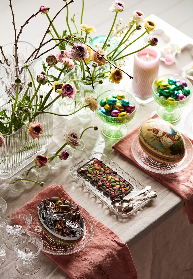 Elegant påskebord med påskeegg fylt med sjokolade, friske blomster og dekorative detaljer. Perfekt inspirasjon til påskefeiring og gaver.