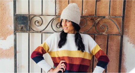 Kvinne i stripet genser og lys strikkelue, stående foran en smijernsport.