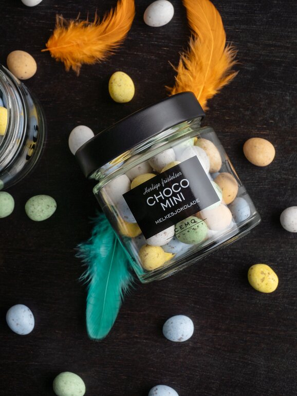 Påskegave med sjokoladeegg, dekorert med fjær og vårfarger – en stilfull gaveidé.
