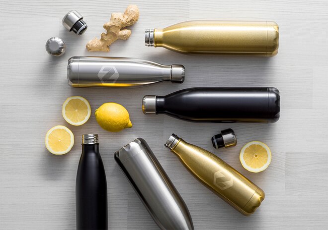 Eksklusive termoflasker i sort, gull og sølv, plassert med sitron og ingefær. Perfekt for varm og kald drikke, ideelle som firmagaver med logotrykk.