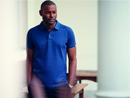 Mann i en blå J. Harvest & Frost-poloskjorte, stående med hendene i lommene.