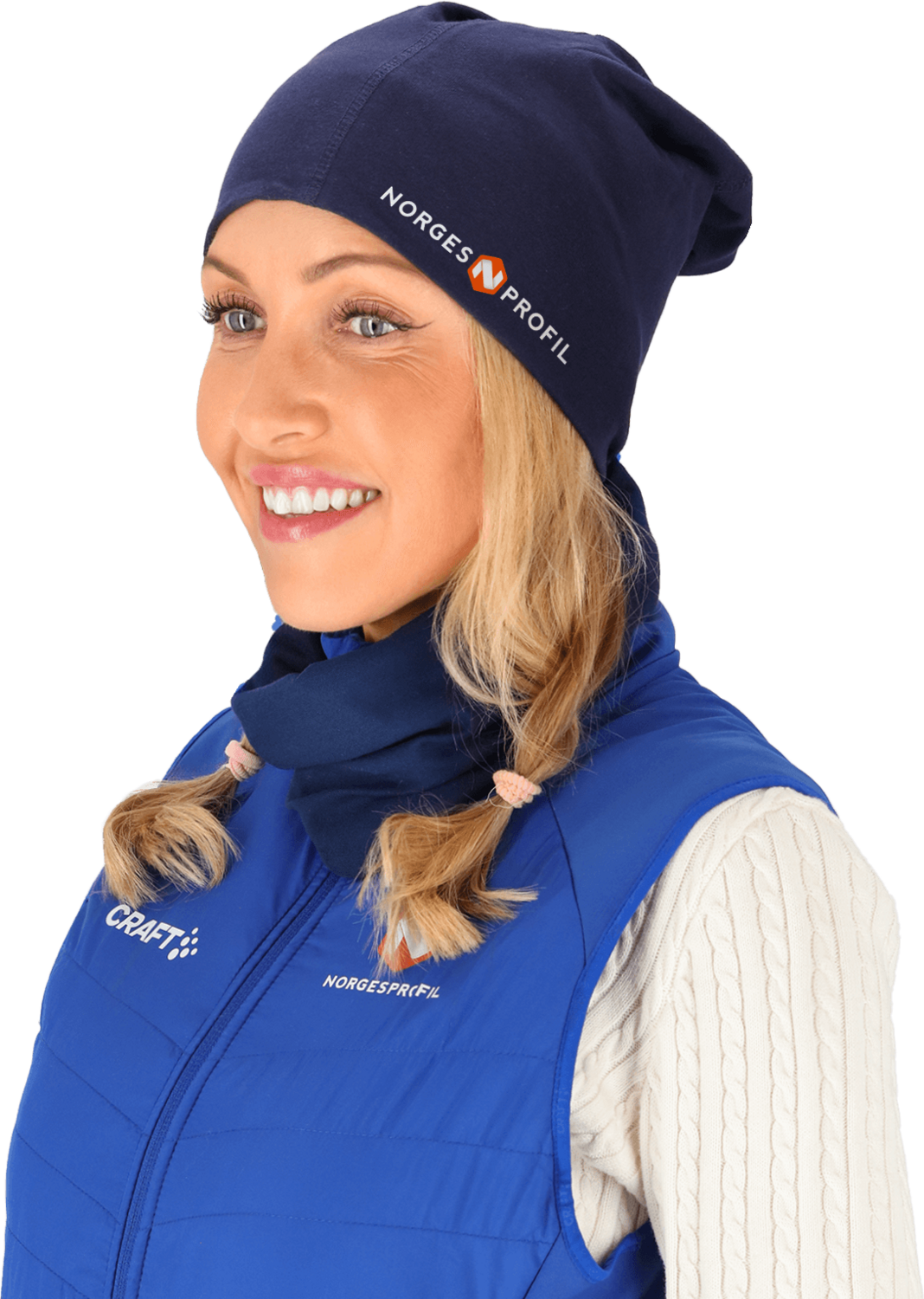 Smilende kvinne iført en marineblå lue med trykt logo og matchende hals, kombinert med en blå vest og hvit strikkegenser. En funksjonell og stilren profilbekledning for kalde dager.