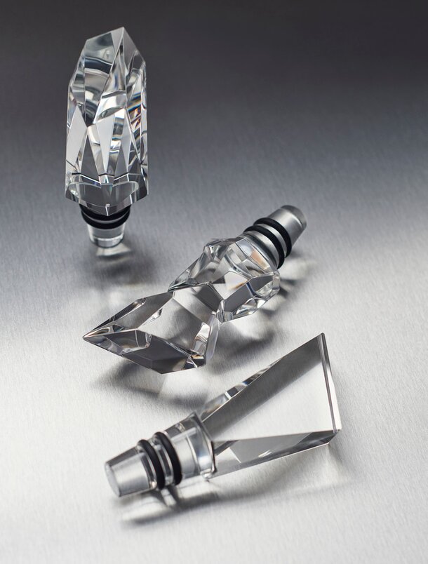 Tre fasetterte Orrefors-krystallkorker i ulik form, liggende på en metallisk overflate.