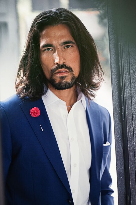 Mann i blå dressjakke og hvit skjorte fra J. Harvest & Frost, med en rød pynteblomst på jakkeslaget.