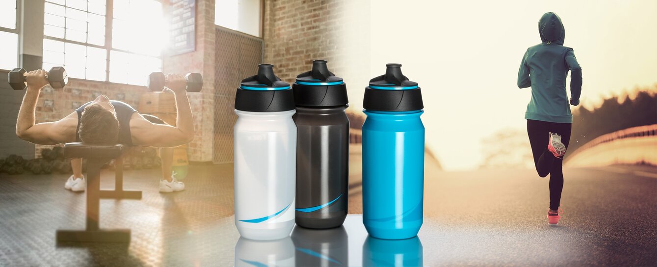 Tre treningsflasker i ulike farger – hvit, svart og blå – står i fokus, med en aktiv livsstil i bakgrunnen. En person trener med vekter innendørs, mens en annen jogger utendørs i solnedgangen. Perfekt som profilartikler for sport og helse.