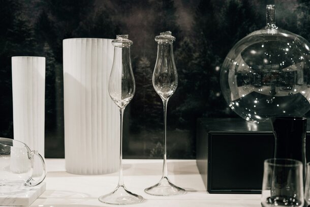 «To høye Orrefors-champagneglass og hvite, sylindriske vaser på et utstillingsbord.