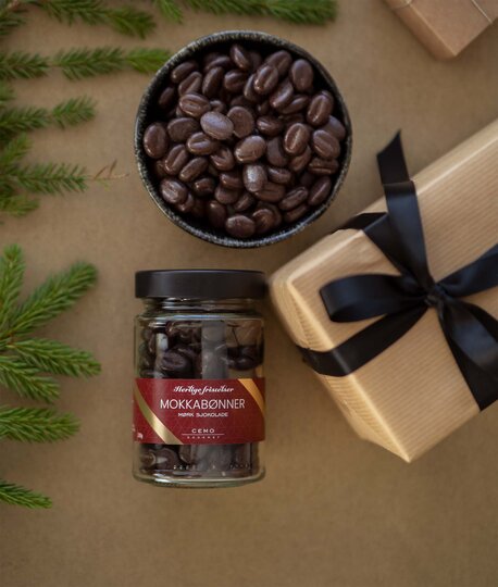 Glass med Cemo mokkabønner ved siden av en gaveeske, pyntet med granbar.