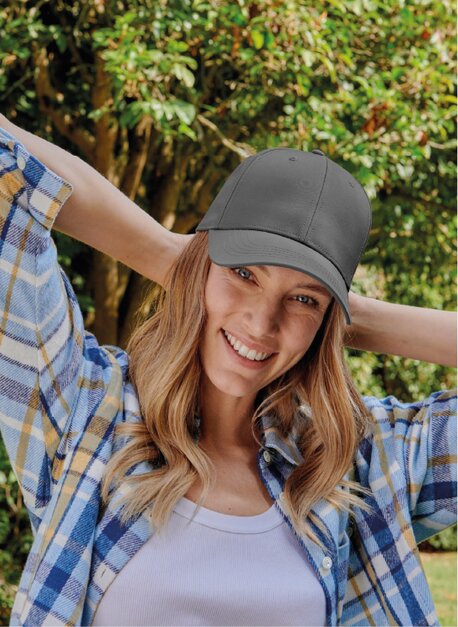 Kvinne i grå caps og rutete skjorte smiler utendørs.