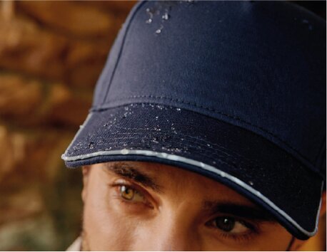 Nærbilde av en mørkeblå caps med vanndråper på bremmen.