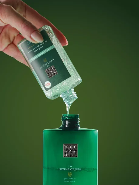 Hånd som heller en påfyllingsflaske med Ritual of Jing-produkt i en større, grønn beholder fra Rituals.