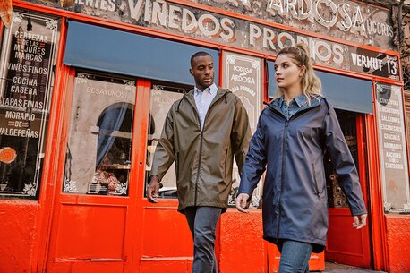 En mann og en kvinne i Roly-regnjakker går foran en rød butikkfasade i en bygate.