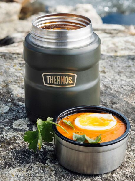 Mørkegrønn Thermos-matbeholder med varm suppe og et halvkokt egg på toppen, fotografert ute ved vannet.