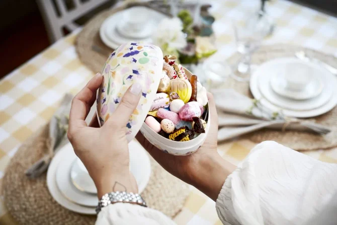 Person åpner et tradisjonelt påskeegg fylt med godteri, sjokolade og påskesnop på et vakkert dekket bord. Perfekt påskegaveidé for både barn og voksne.
