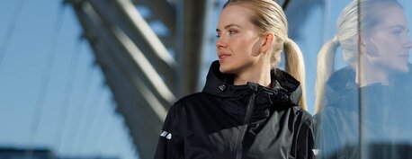 Kvinne i sort jakke fra YOU® kolleksjonen, reflektert i en glassfasade 