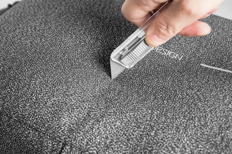 Nærbilde av en hånd som tester en kniv mot en XD Design-ryggsekk for å demonstrere skjærebestandig materiale.