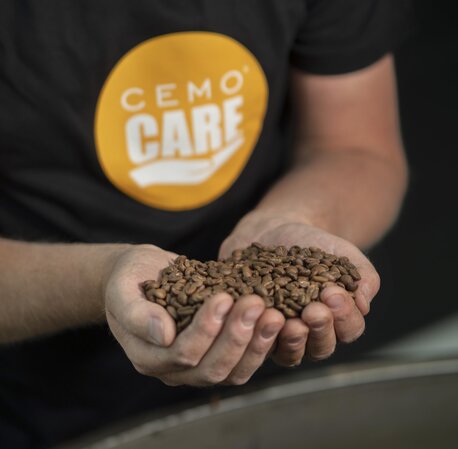 Nærbilde av en person i Cemo Care-T-skjorte som holder en håndfull nybrente kaffebønner.
