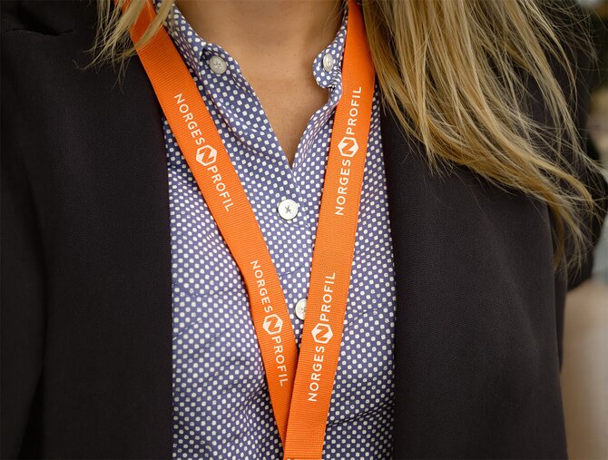 Oransje nøkkelbånd med firmalogo båret av en person i businessantrekk. Ideell profileringsartikkel for messer, events og ansatte.