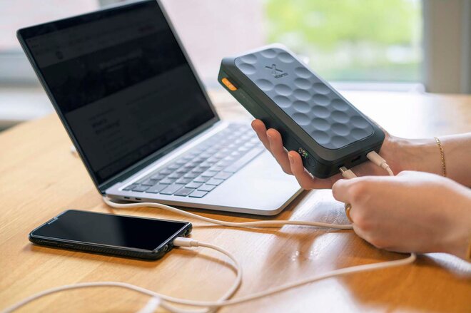 Moderne trådløs powerbank med strukturert overflate, holdt av en person ved en laptop. Praktisk og stilren firmagave med mulighet for logotrykk.