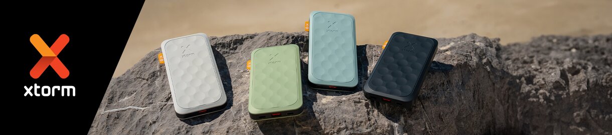 Fire Xtorm-powerbanks i ulike farger, plassert på en stein, ved siden av Xtorm-logoen