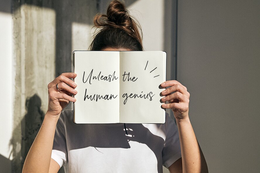 Kvinne holder opp en åpen Moleskine-notatbok med teksten ‘Unleash the human genius’.