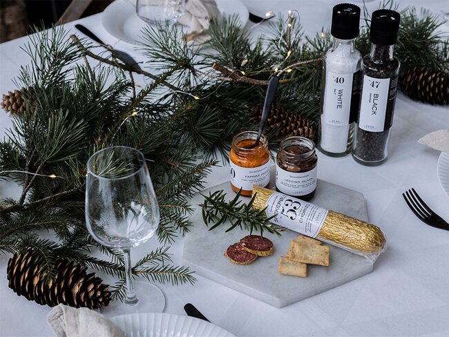 Matgaver – delikat gavepakke med spekepølse, kjeks, paprika pesto, oliven og krydder på julepyntet bord