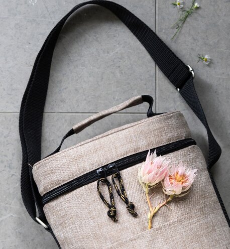 Naturlig og stilfull kjølebag i linmateriale fra Sagaform, med svarte reimer og blomsterdekorasjon på lommen.