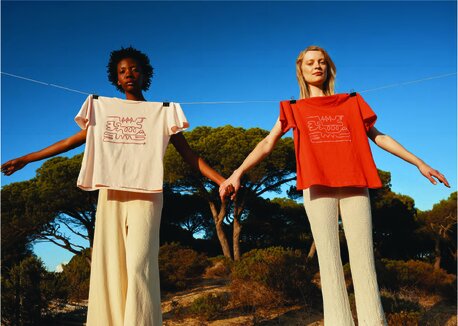 To kvinner i lyse bukser holder hender under en klessnor med rosa og rød Iqoniq-T-skjorte.