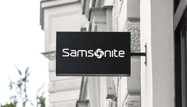 Svart, rektangulært skilt med hvit Samsonite-logo, montert på en bybygning.