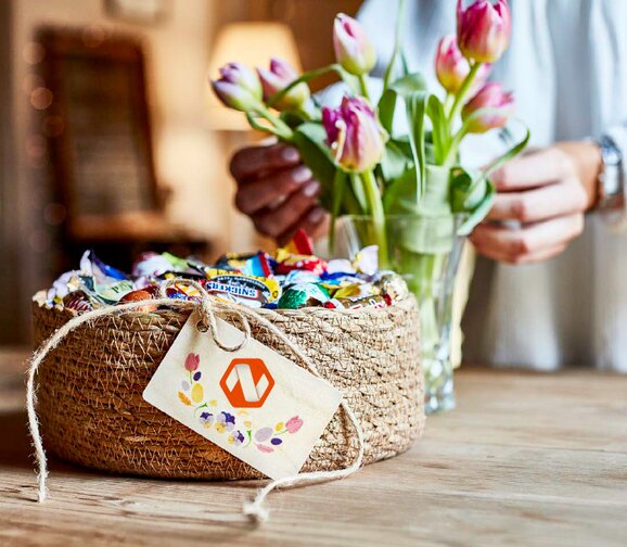 Gavekurv fylt med sjokolade og godteri, pyntet med vårblomster – en smakfull og elegant påskegave.