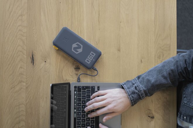 Sort powerbank med digitalt display koblet til en bærbar PC via USB. Kraftig og praktisk profileringsartikkel for reiser og kontorbruk.